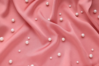 Photo of Many elegant pearls on pink fabric, top view