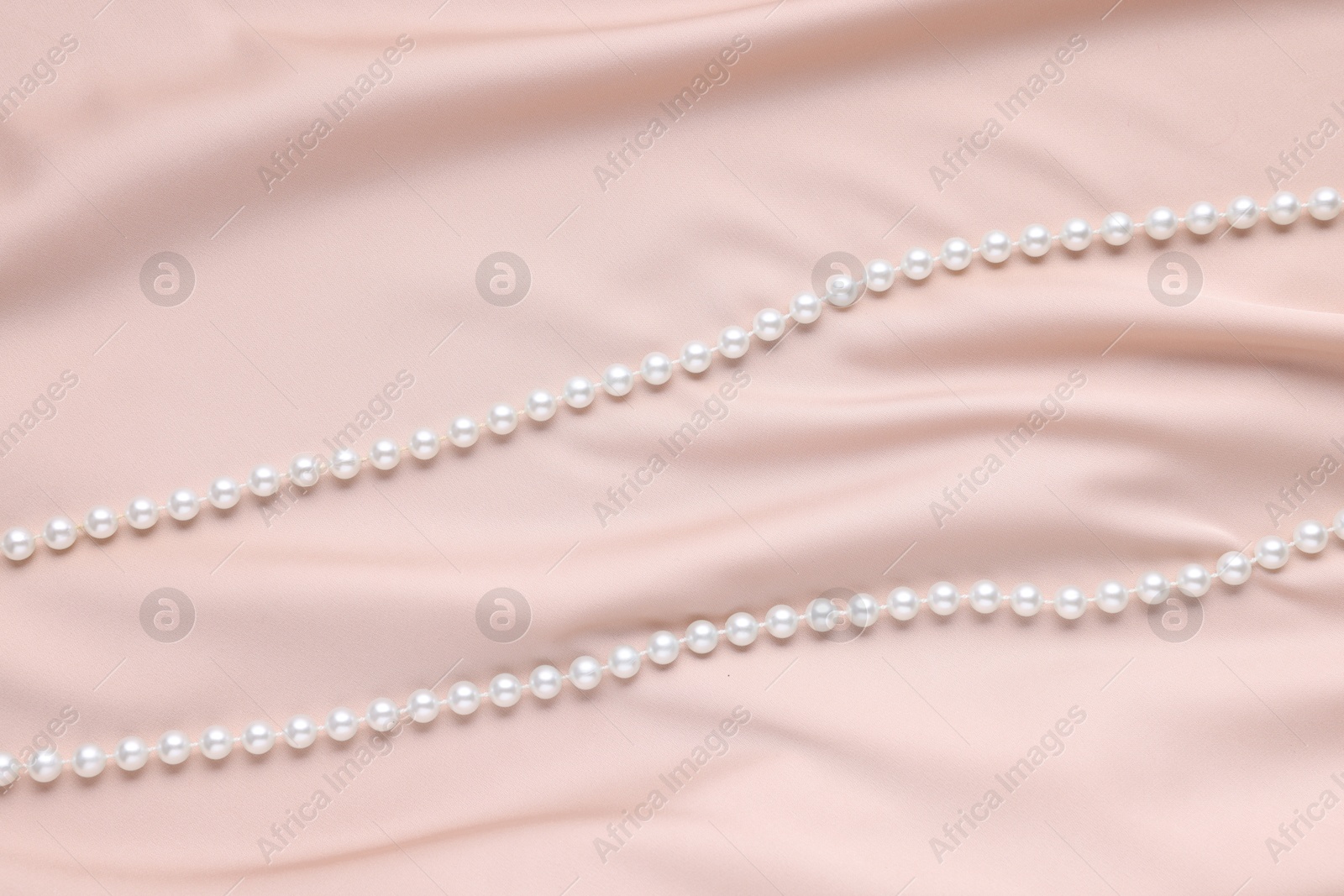 Photo of Elegant pearl necklace on beige fabric, top view