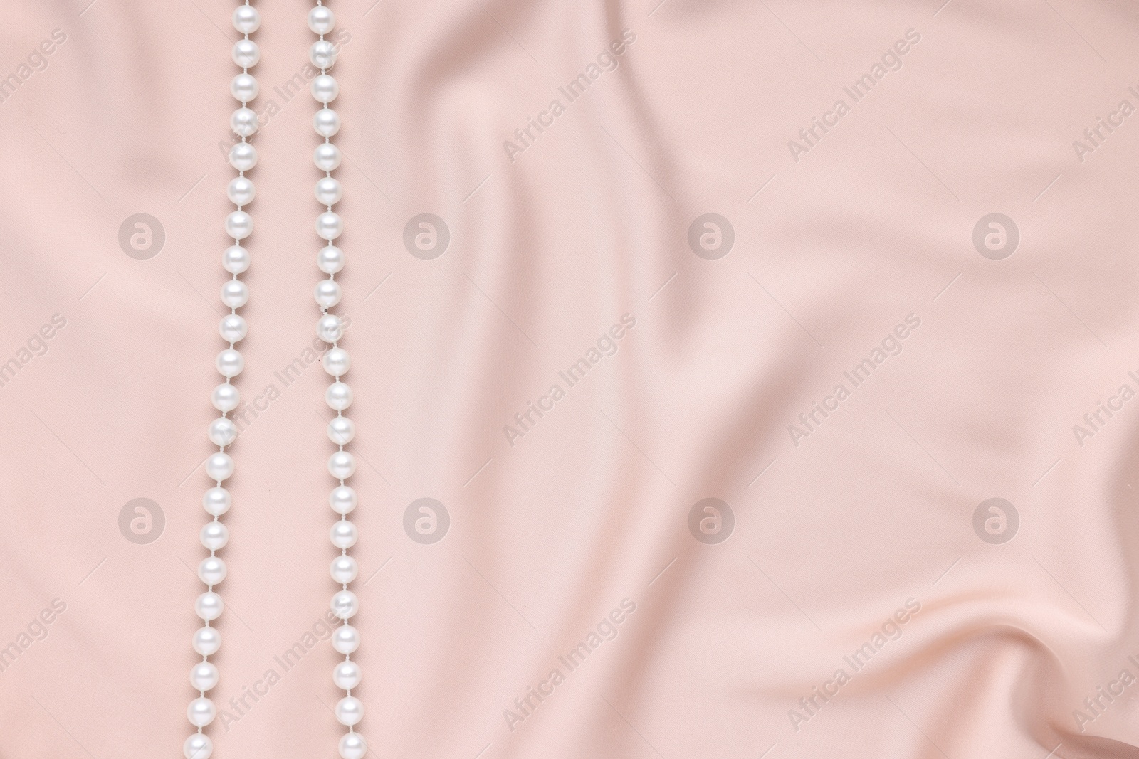 Photo of Elegant pearl necklace on beige fabric, top view. Space for text