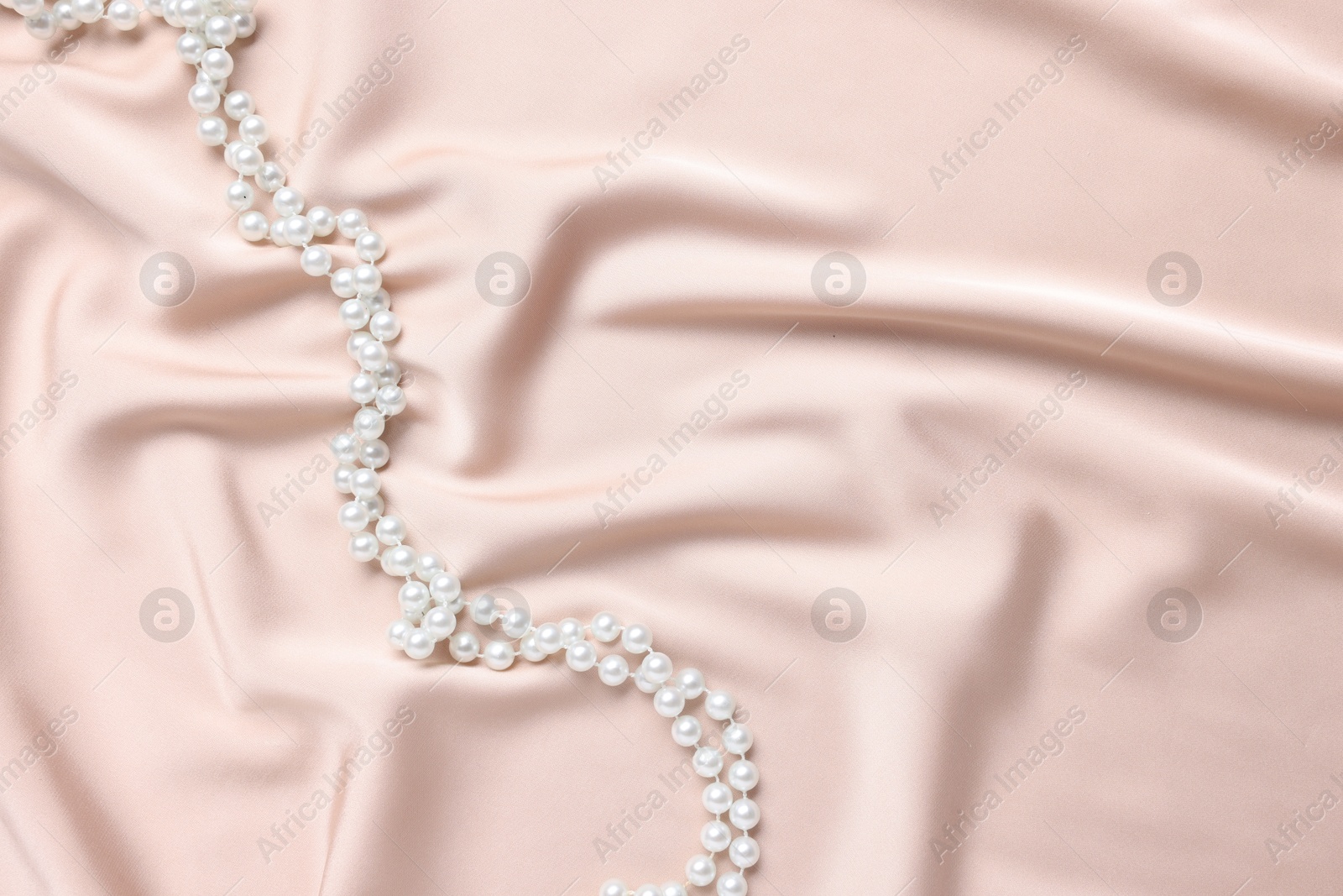 Photo of Elegant pearl necklace on beige fabric, top view. Space for text