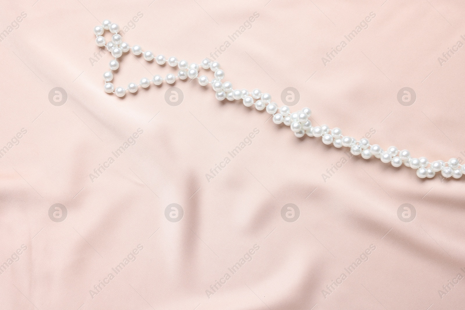 Photo of Elegant pearl necklace on beige fabric, top view. Space for text