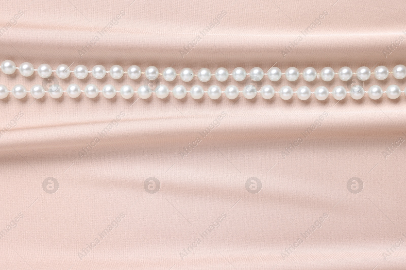 Photo of Elegant pearl necklace on beige fabric, top view. Space for text