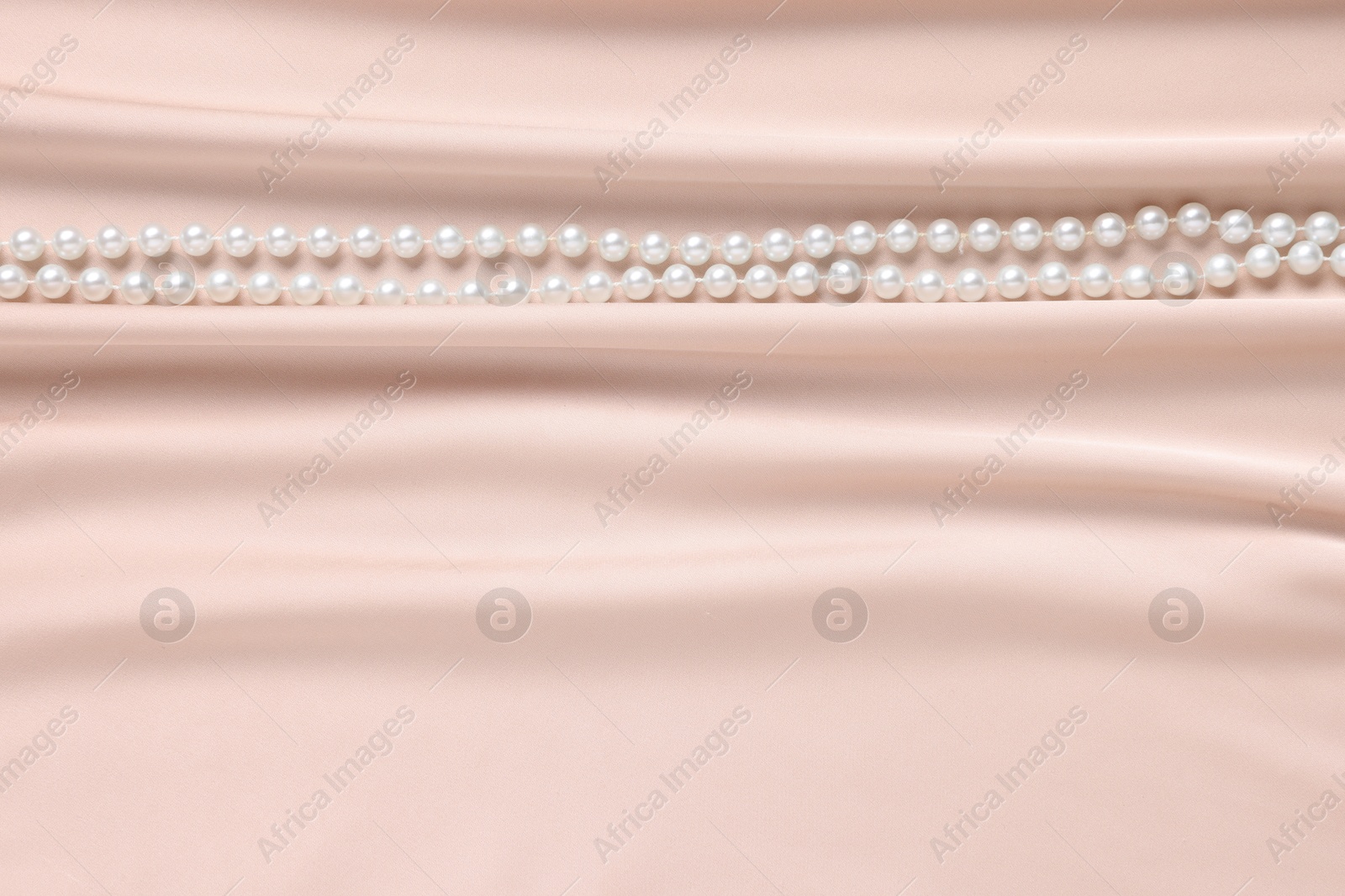 Photo of Elegant pearl necklace on beige fabric, top view. Space for text