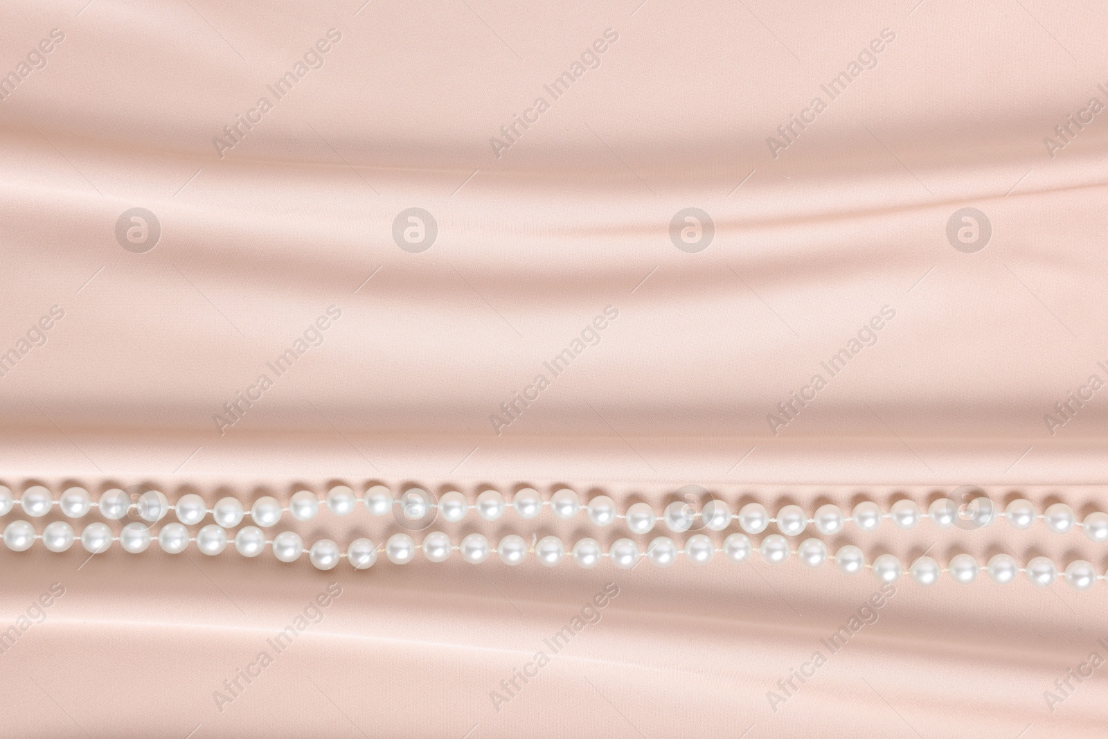 Photo of Elegant pearl necklace on beige fabric, top view. Space for text