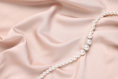 Photo of Elegant pearl necklace on beige fabric, top view. Space for text