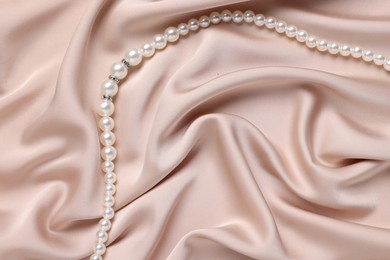 Photo of Elegant pearl necklace on beige fabric, top view