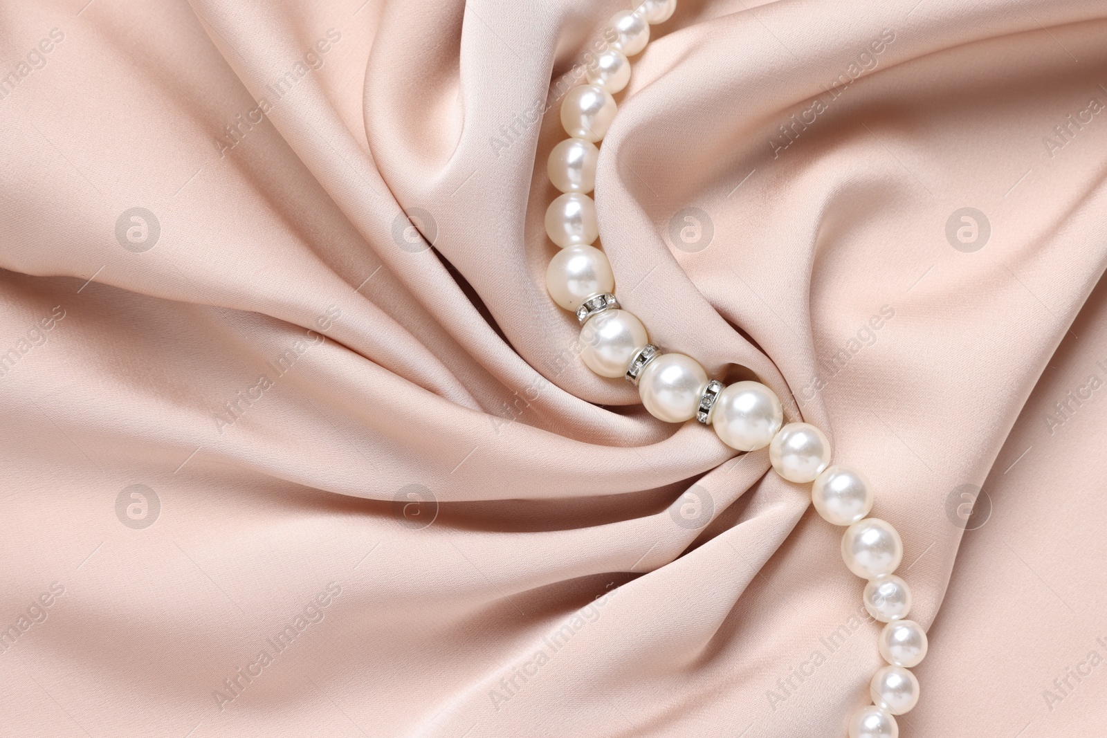 Photo of Elegant pearl necklace on beige fabric, top view