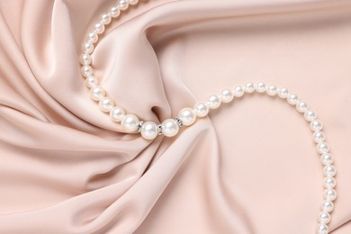 Photo of Elegant pearl necklace on beige fabric, top view