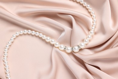 Photo of Elegant pearl necklace on beige fabric, top view