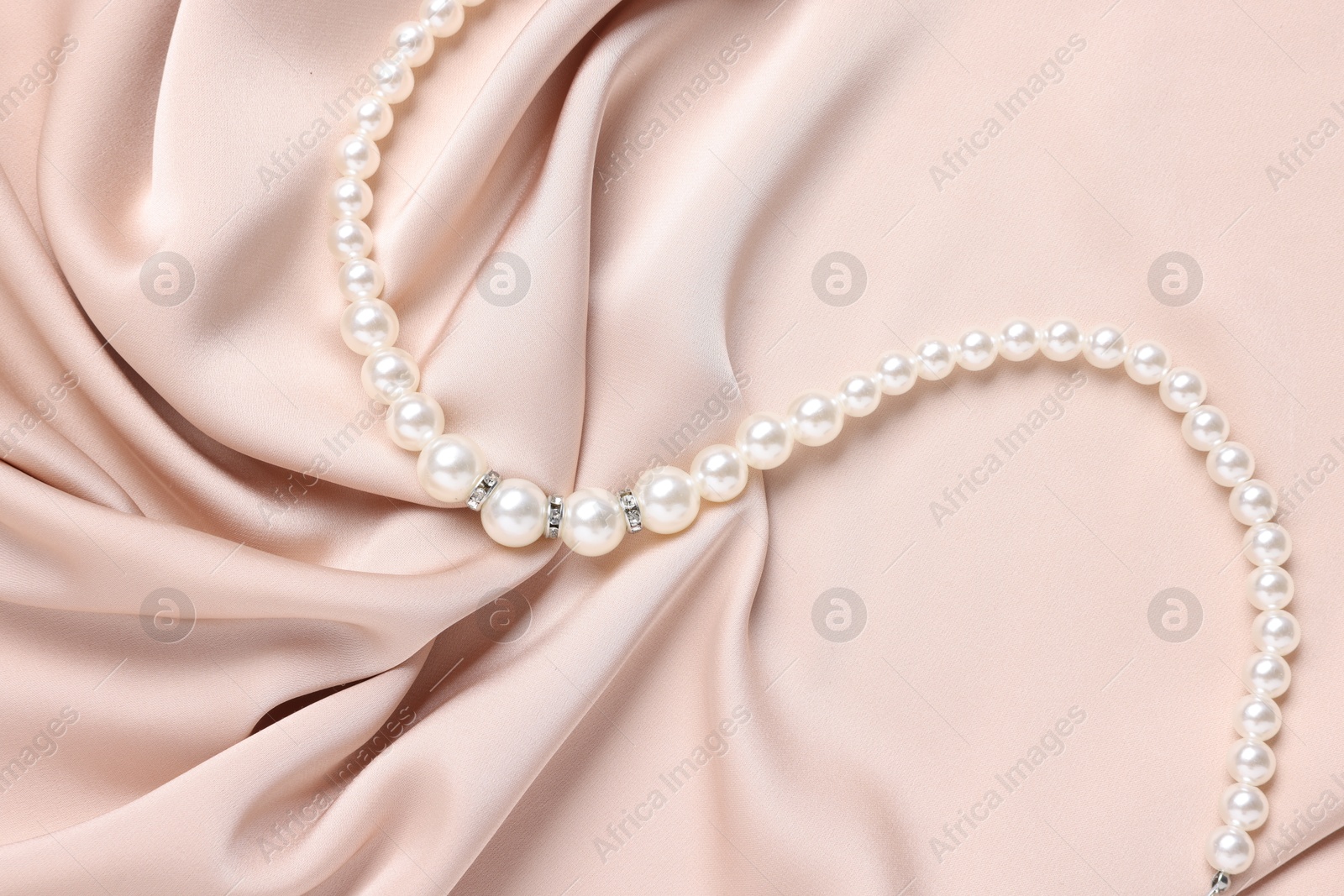 Photo of Elegant pearl necklace on beige fabric, top view