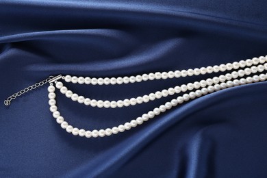 Photo of Elegant pearl necklace on dark blue fabric, top view