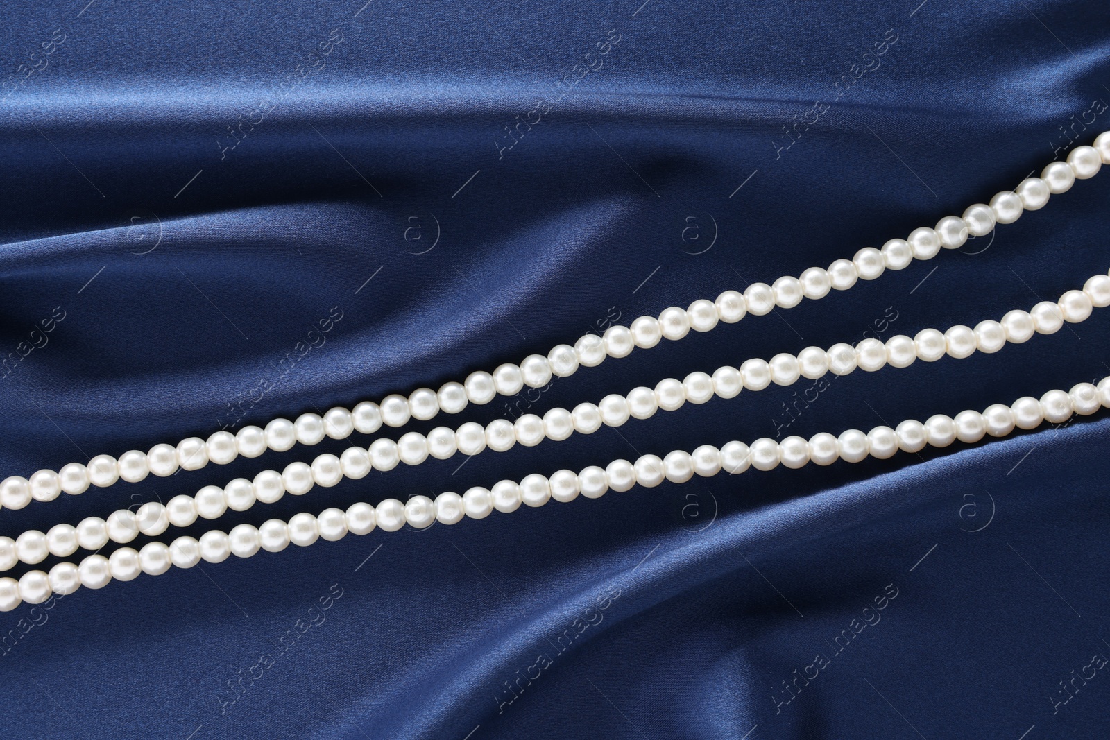 Photo of Elegant pearl necklace on dark blue fabric, top view