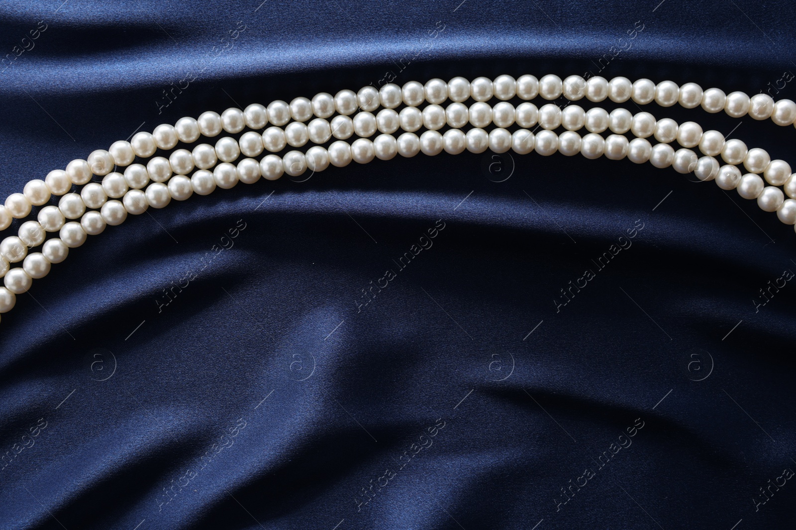 Photo of Elegant pearl necklace on dark blue fabric, top view. Space for text