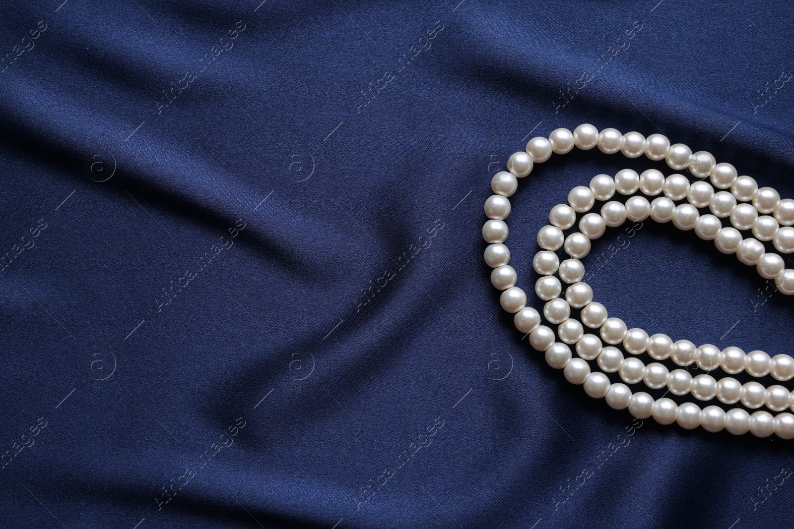 Photo of Elegant pearl necklace on dark blue fabric, top view. Space for text