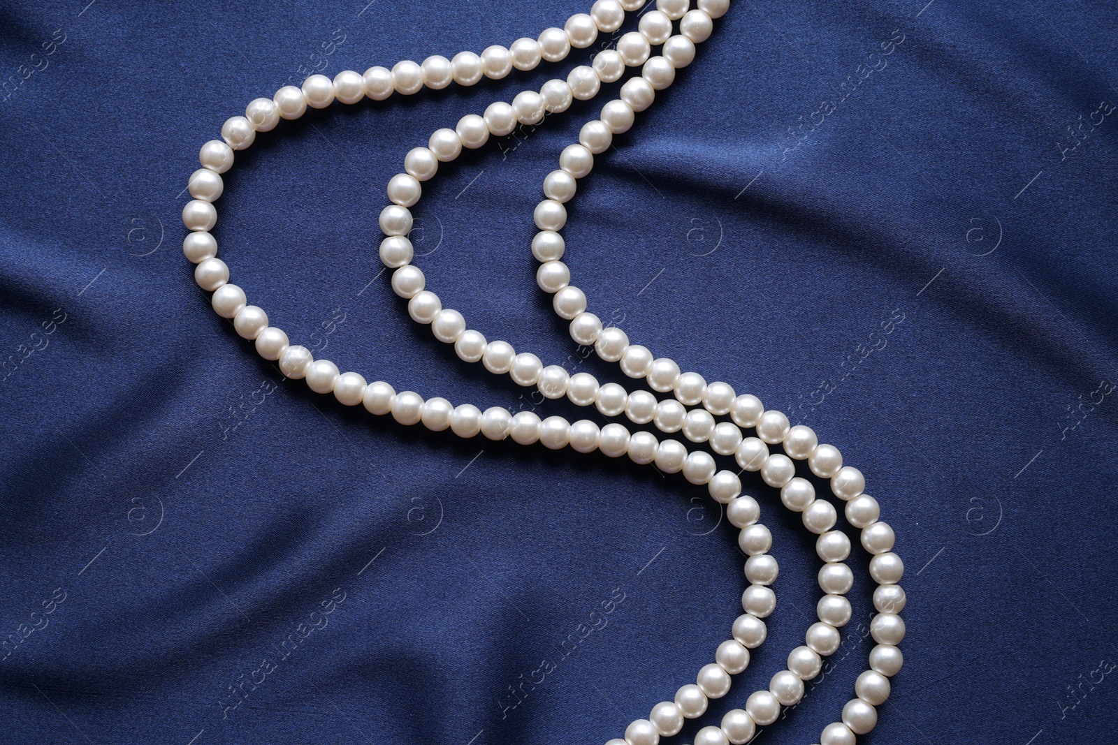 Photo of Elegant pearl necklace on dark blue fabric, top view