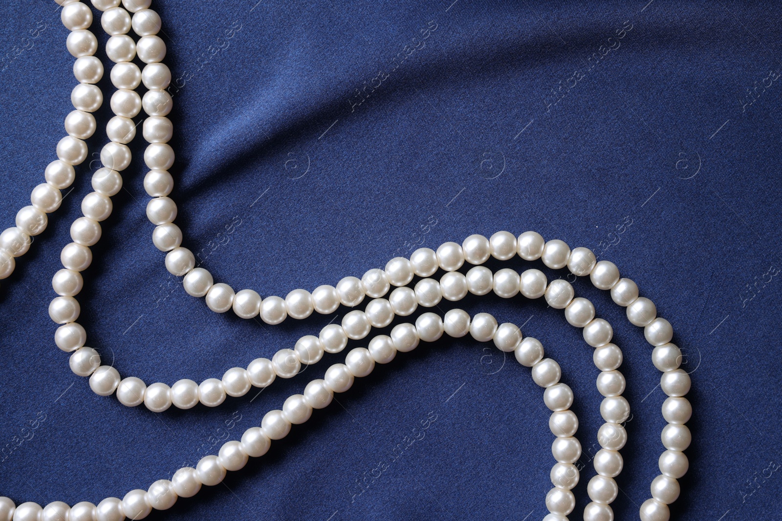 Photo of Elegant pearl necklace on dark blue fabric, top view