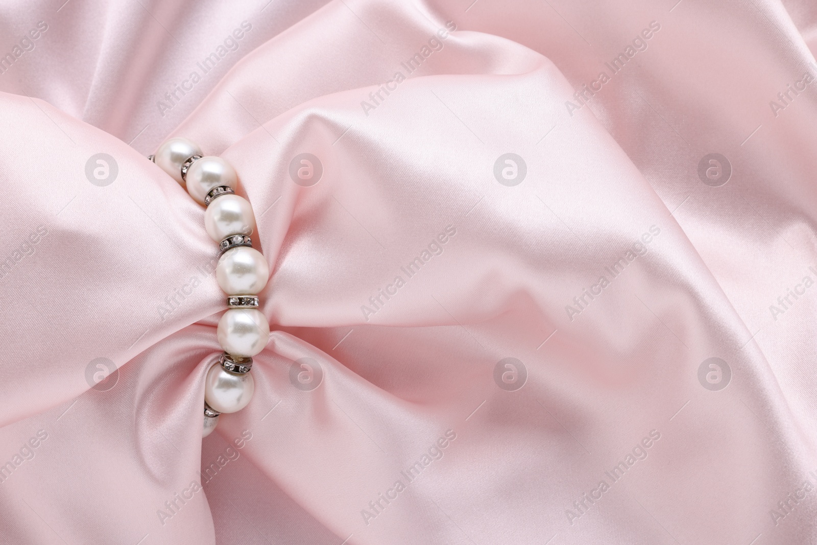 Photo of Elegant pearl bracelet on pink fabric, closeup. Space for text