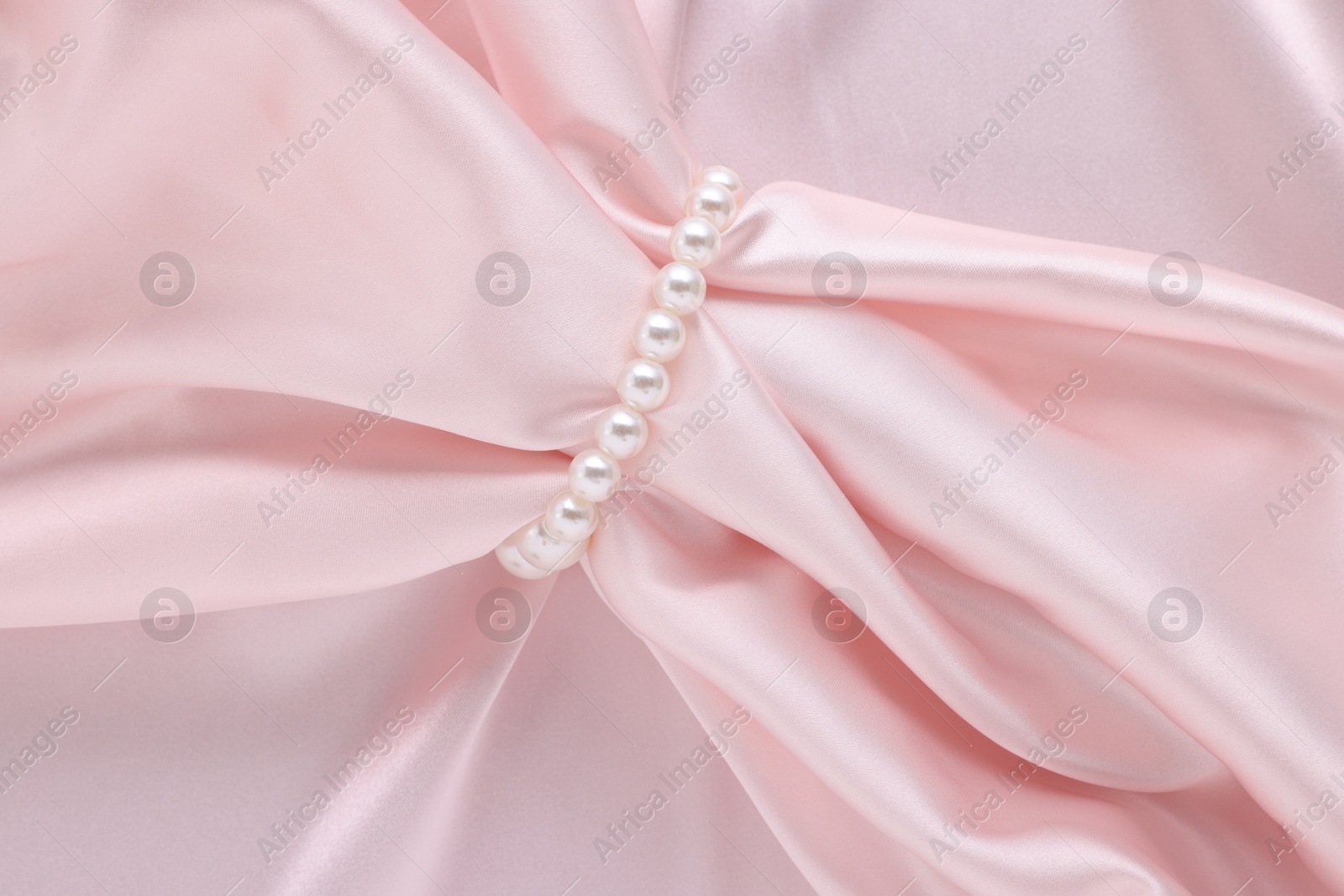 Photo of Elegant pearl bracelet on pink fabric, top view