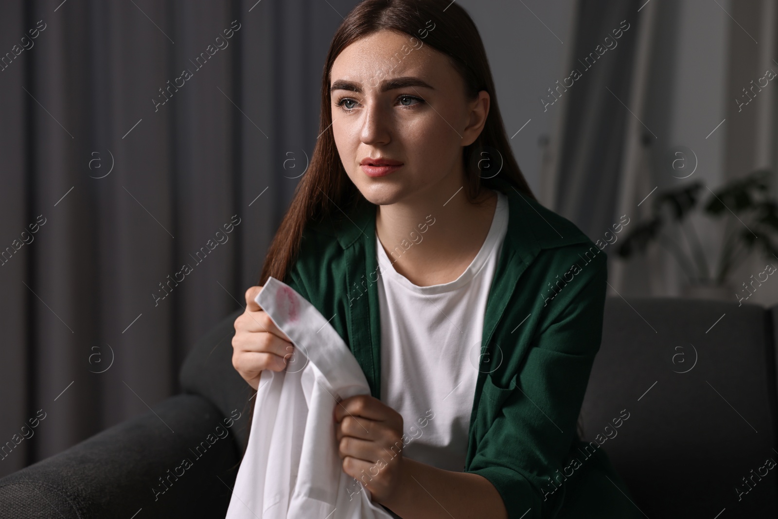 Photo of Frustrated wife holding shirt with lipstick marks as proof of her unfaithful husband at home