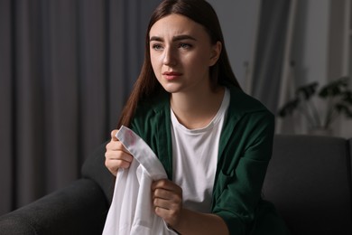 Frustrated wife holding shirt with lipstick marks as proof of her unfaithful husband at home