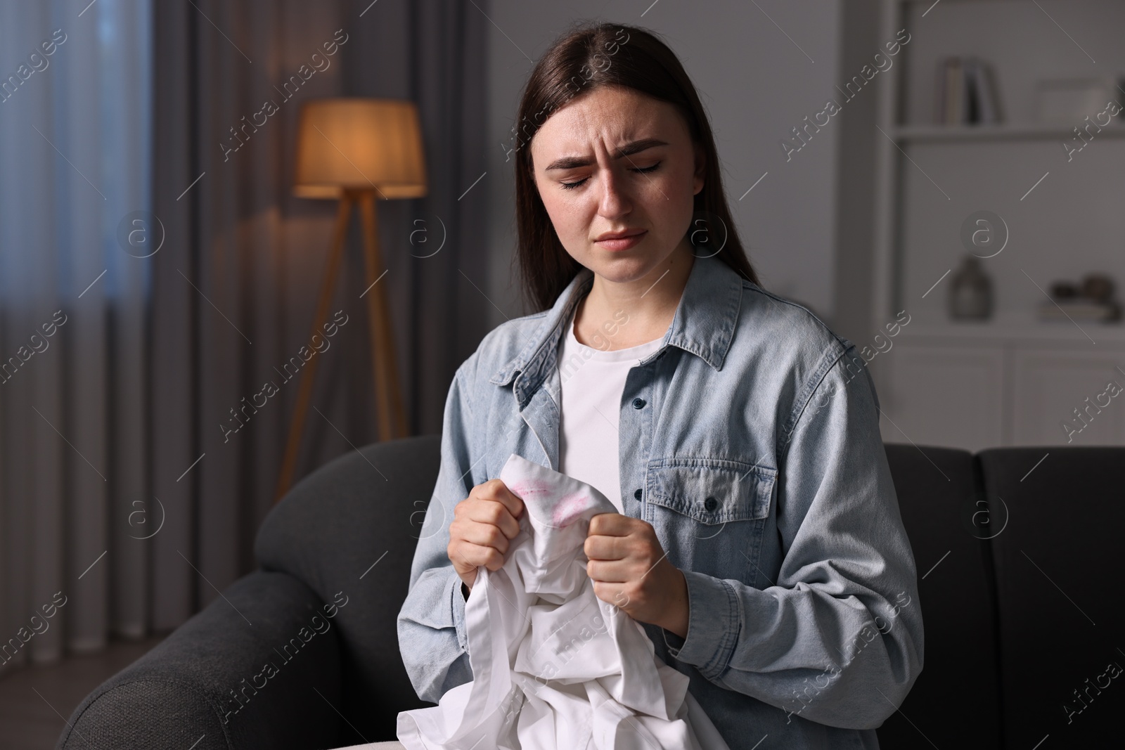 Photo of Frustrated wife holding shirt with lipstick marks as proof of her unfaithful husband at home