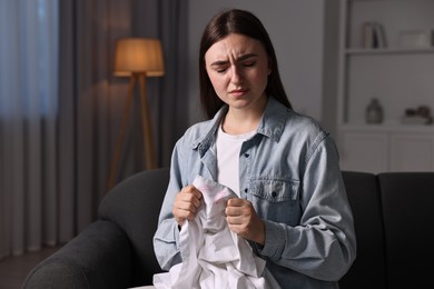 Frustrated wife holding shirt with lipstick marks as proof of her unfaithful husband at home