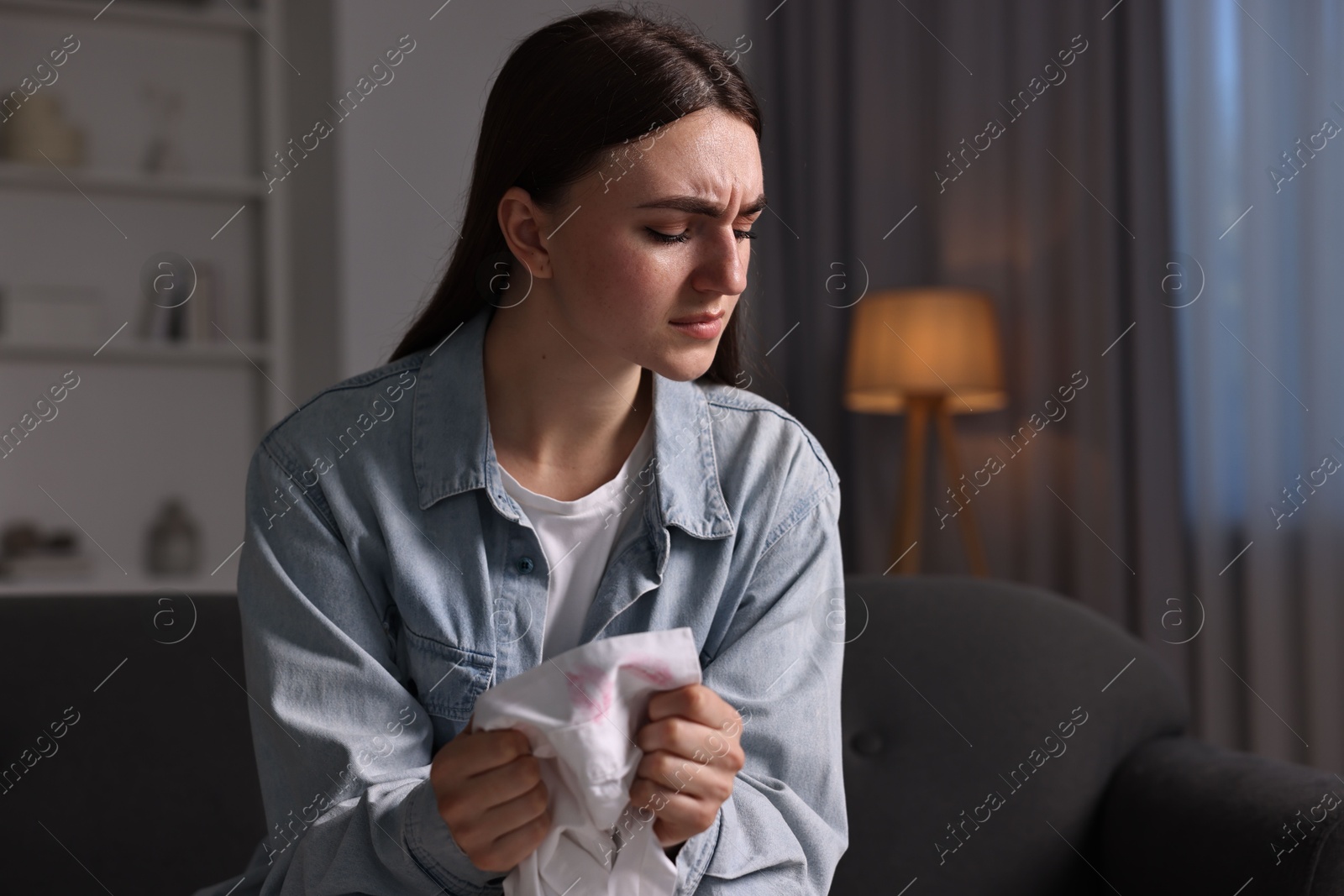 Photo of Frustrated wife holding shirt with lipstick marks as proof of her unfaithful husband at home