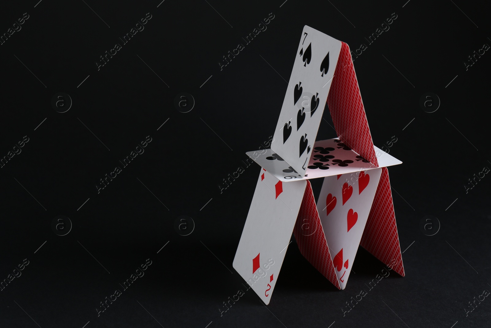 Photo of House of playing cards on black background, space for text