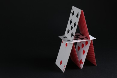 Photo of House of playing cards on black background, space for text