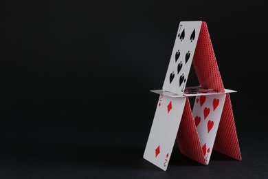 Photo of House of playing cards on black background, space for text