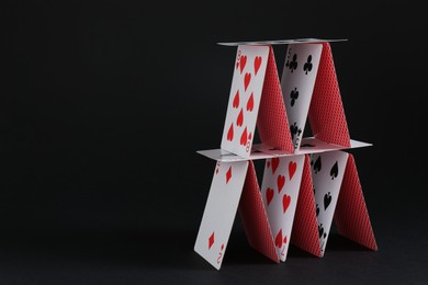 Photo of House of playing cards on black background, space for text