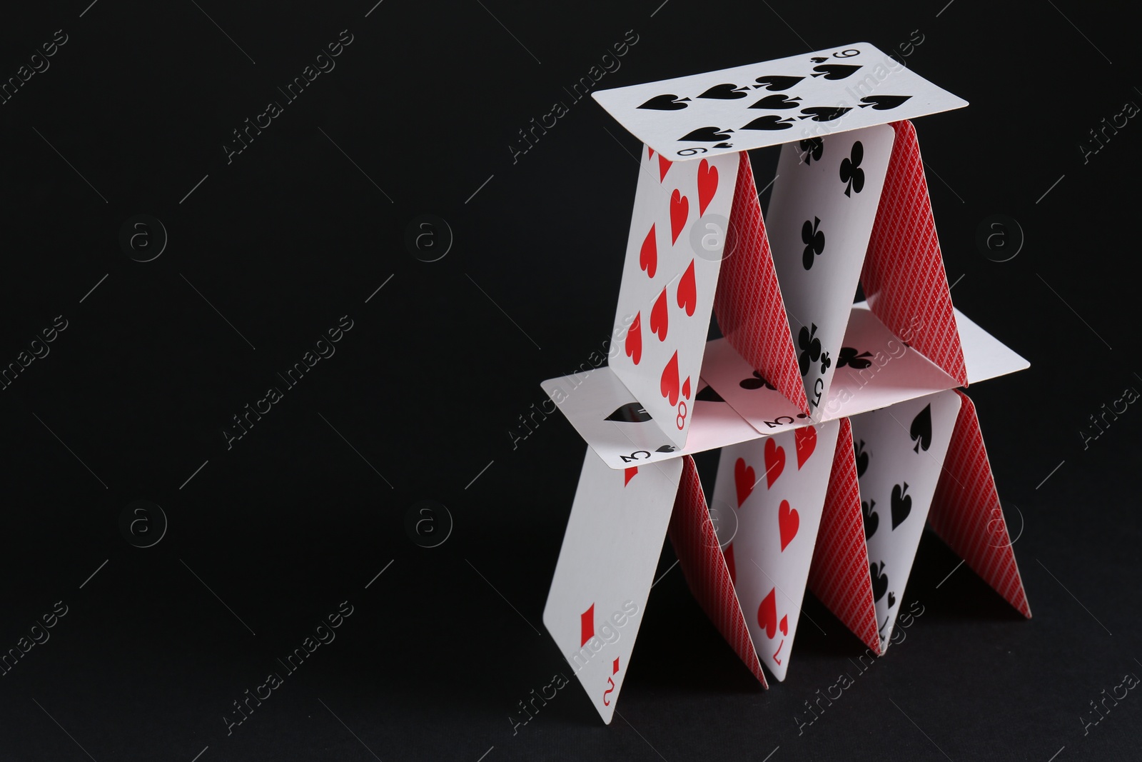 Photo of House of playing cards on black background, space for text