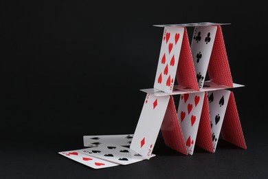 Photo of House of playing cards on black background, space for text