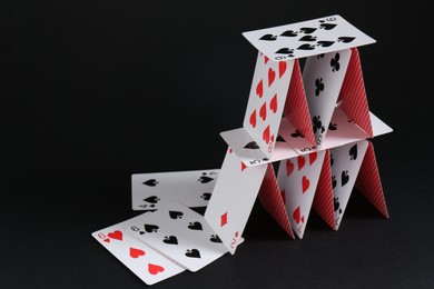 Photo of House of playing cards on black background, space for text