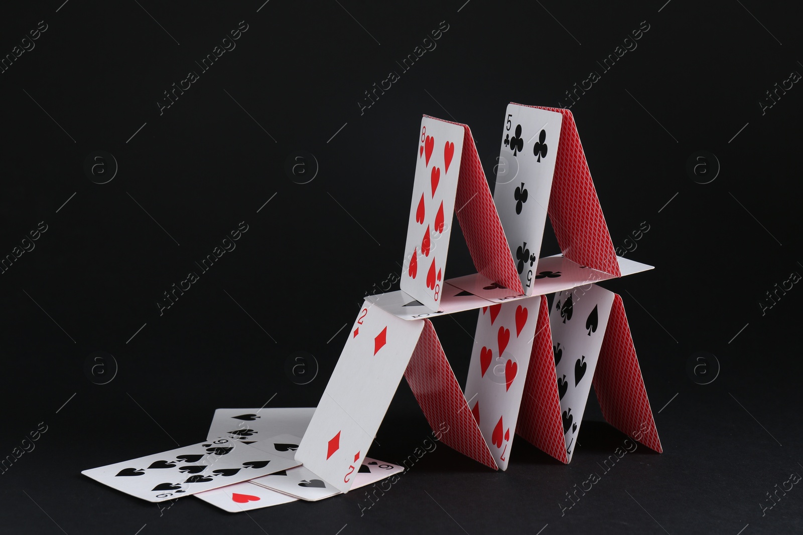 Photo of House of playing cards on black background, space for text