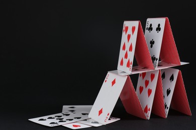 Photo of House of playing cards on black background, space for text