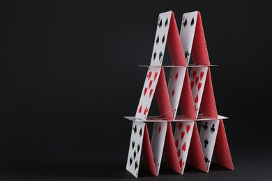 Photo of House of playing cards on black background, space for text