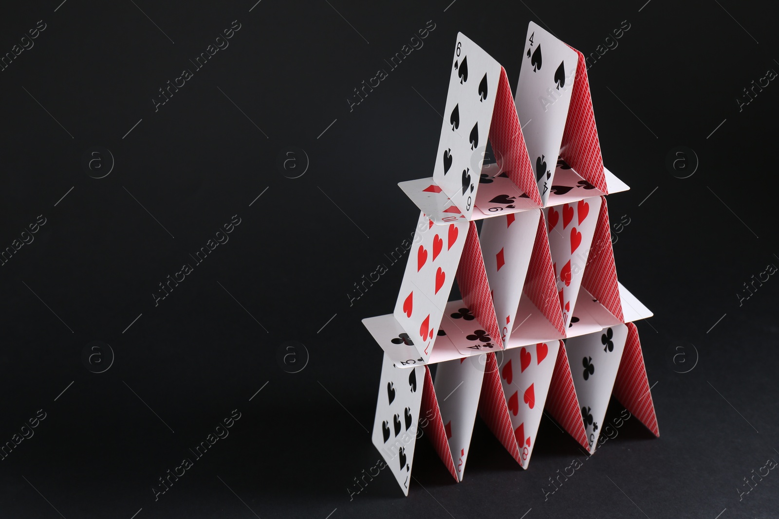 Photo of House of playing cards on black background, space for text