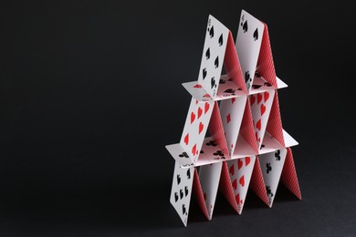 Photo of House of playing cards on black background, space for text