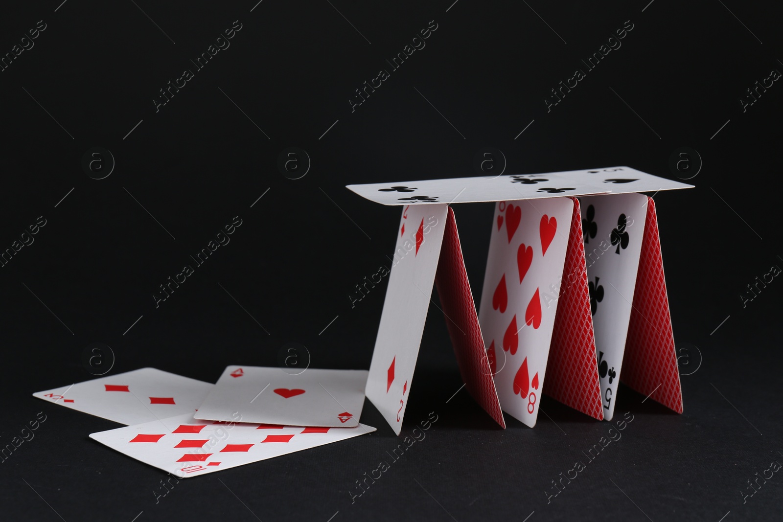 Photo of Collapsed house of playing cards on black background