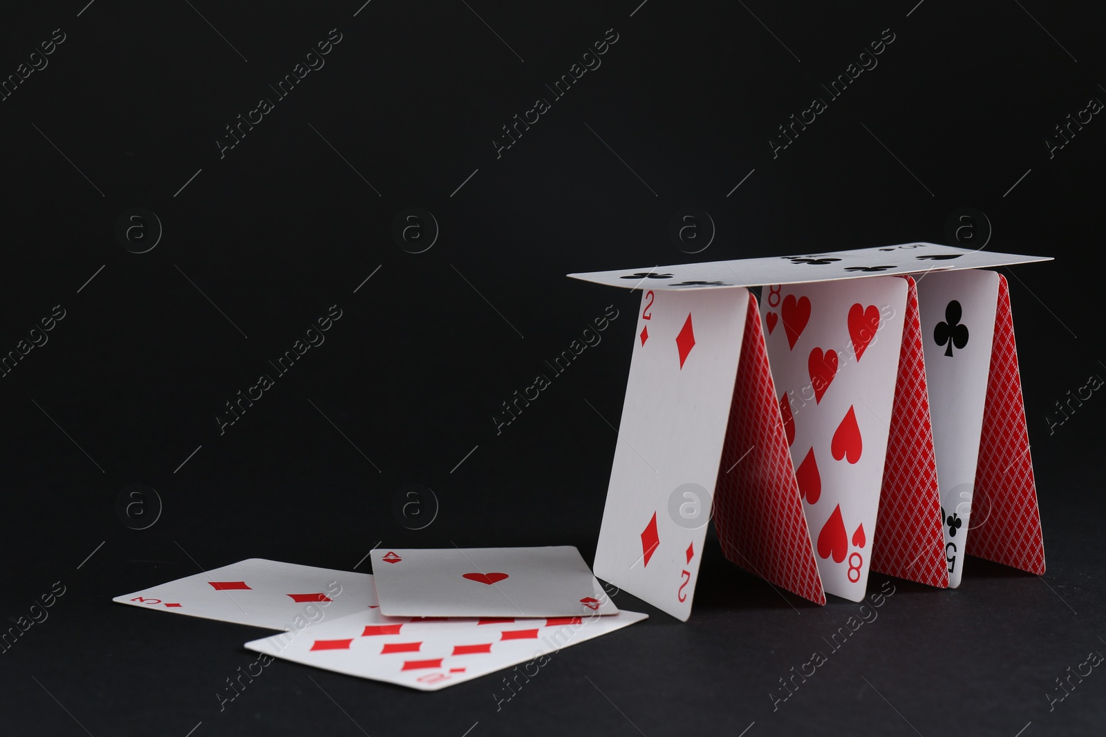 Photo of Collapsed house of playing cards on black background, space for text