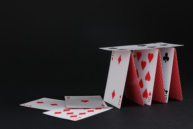 Photo of Collapsed house of playing cards on black background, space for text