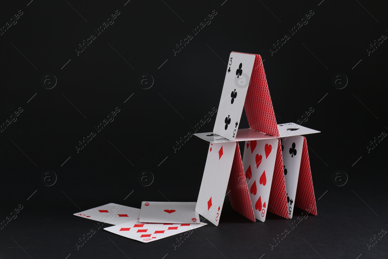 Photo of House of playing cards on black background, space for text