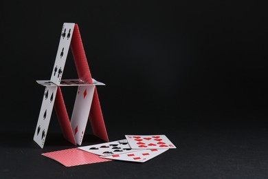 Photo of House of playing cards on black background, space for text