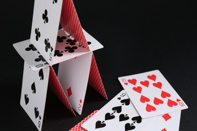 Photo of House of playing cards on black background, space for text