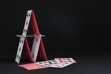 Photo of House of playing cards on black background, space for text