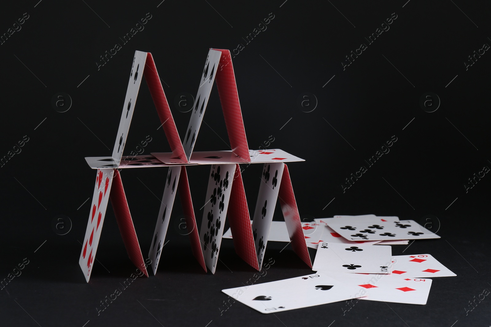 Photo of House of playing cards on black background, space for text