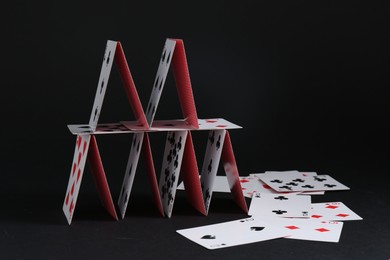 Photo of House of playing cards on black background, space for text