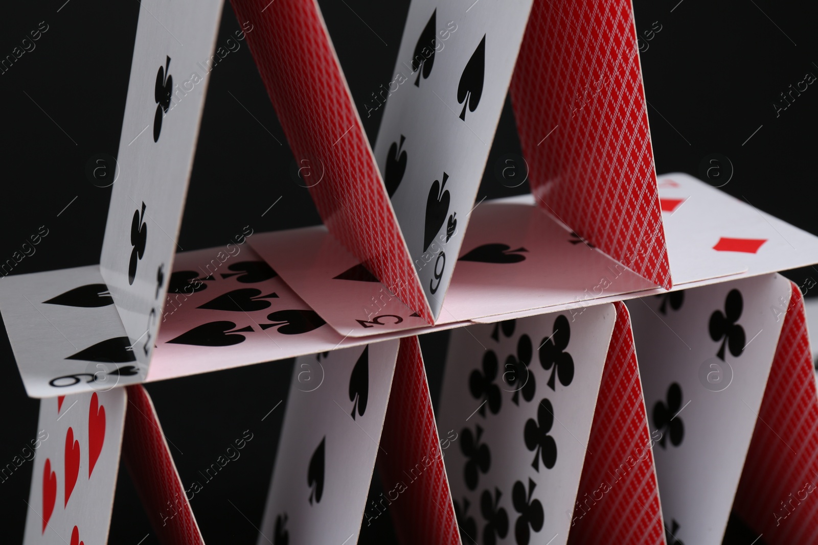 Photo of House of playing cards on black background, closeup