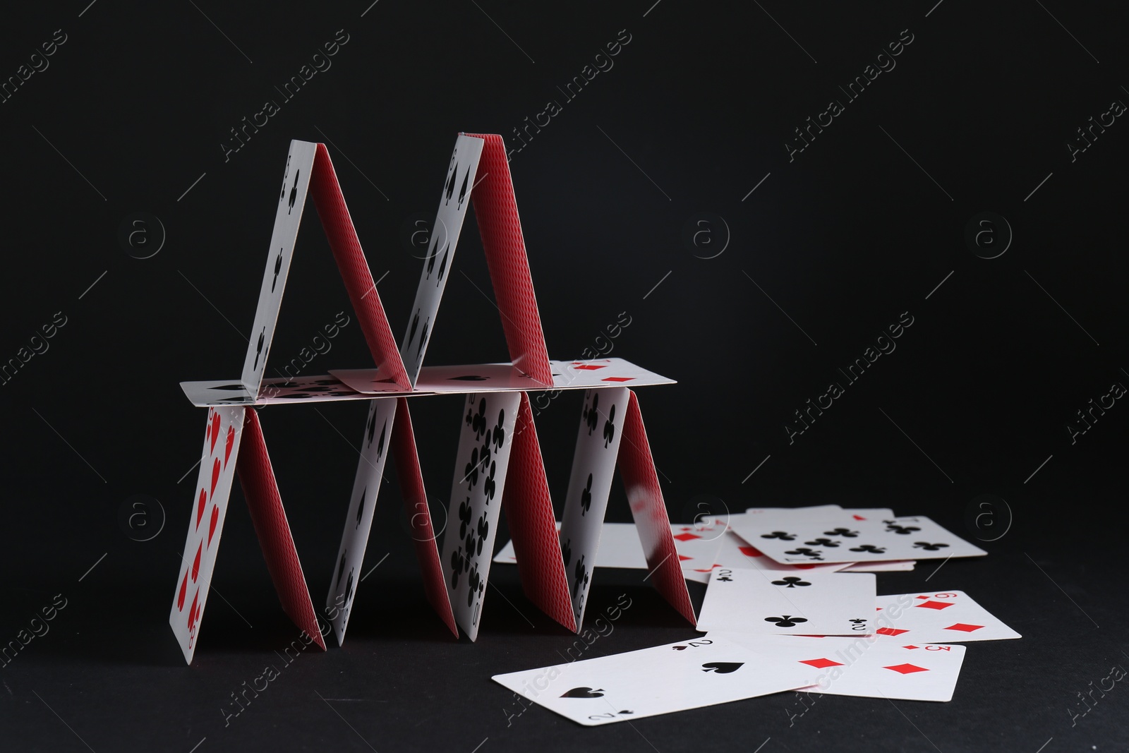 Photo of House of playing cards on black background, space for text